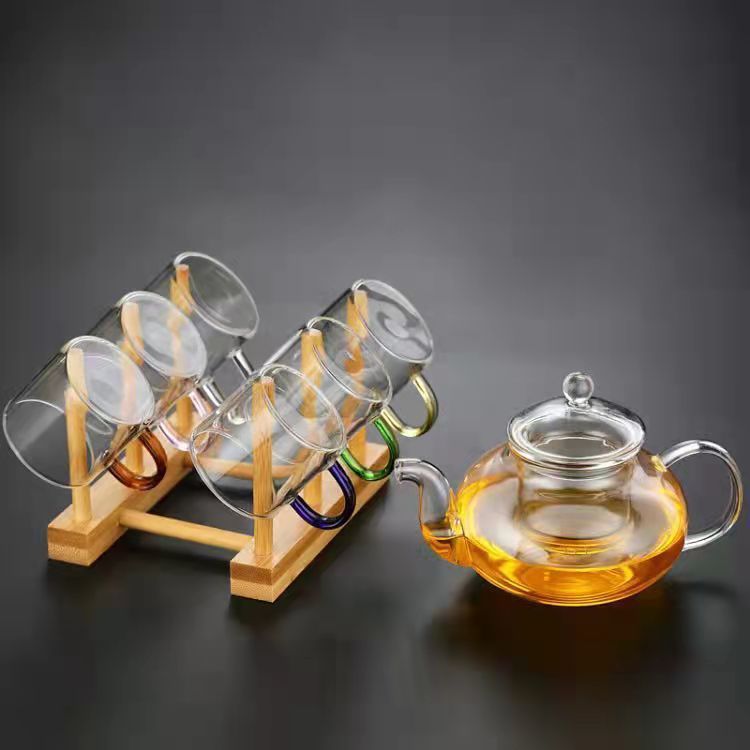 A beautifully arranged Thick Glass Transparent Tea Set, featuring a minimalist design with high borosilicate glass. The set includes six elegant tea cups and a matching cup holder, perfect for serving tea. Available in various sizes and styles, including transparent and colorful options with long spout pots.