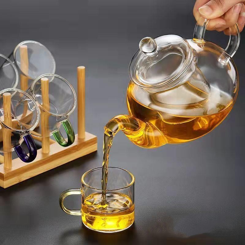 A beautifully arranged Thick Glass Transparent Tea Set, featuring a minimalist design with high borosilicate glass. The set includes six elegant tea cups and a matching cup holder, perfect for serving tea. Available in various sizes and styles, including transparent and colorful options with long spout pots.