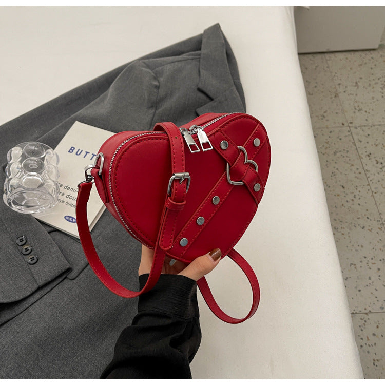 Cute heart-shaped shoulder messenger bag made of soft PU material, featuring a zipper change bag inside. Available in black, cream white, silver, and wine red, with a single shoulder strap and an urban simplicity style for everyday use.