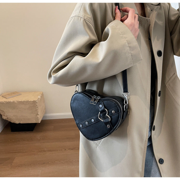 Cute heart-shaped shoulder messenger bag made of soft PU material, featuring a zipper change bag inside. Available in black, cream white, silver, and wine red, with a single shoulder strap and an urban simplicity style for everyday use.