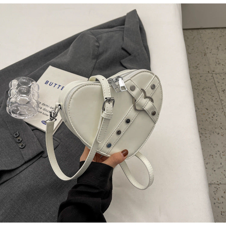 Cute heart-shaped shoulder messenger bag made of soft PU material, featuring a zipper change bag inside. Available in black, cream white, silver, and wine red, with a single shoulder strap and an urban simplicity style for everyday use.