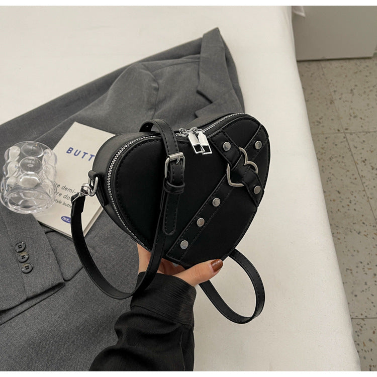 Cute heart-shaped shoulder messenger bag made of soft PU material, featuring a zipper change bag inside. Available in black, cream white, silver, and wine red, with a single shoulder strap and an urban simplicity style for everyday use.