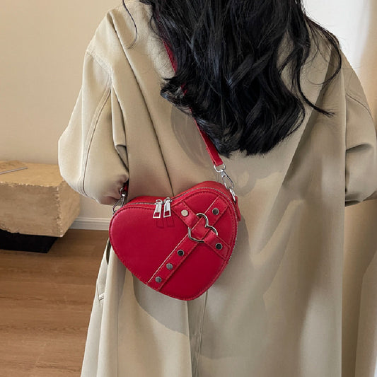 Cute heart-shaped shoulder messenger bag made of soft PU material, featuring a zipper change bag inside. Available in black, cream white, silver, and wine red, with a single shoulder strap and an urban simplicity style for everyday use.