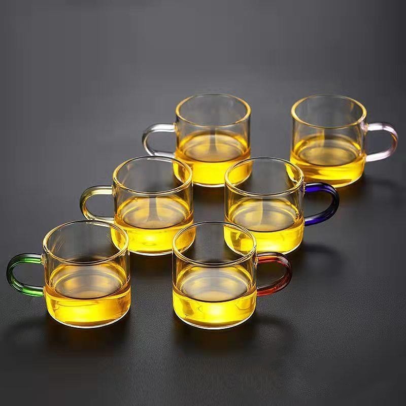A beautifully arranged Thick Glass Transparent Tea Set, featuring a minimalist design with high borosilicate glass. The set includes six elegant tea cups and a matching cup holder, perfect for serving tea. Available in various sizes and styles, including transparent and colorful options with long spout pots.