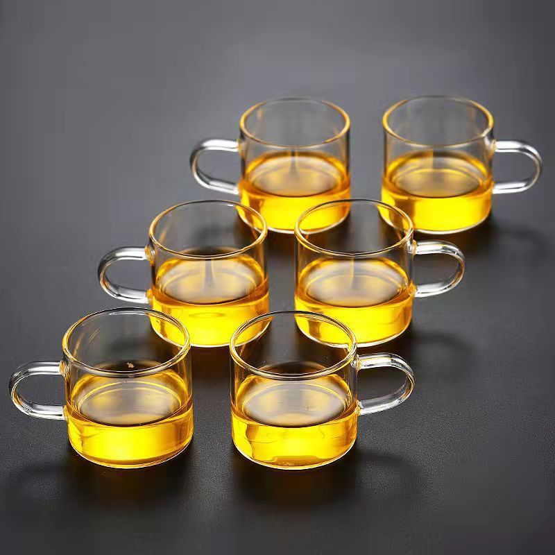 A beautifully arranged Thick Glass Transparent Tea Set, featuring a minimalist design with high borosilicate glass. The set includes six elegant tea cups and a matching cup holder, perfect for serving tea. Available in various sizes and styles, including transparent and colorful options with long spout pots.