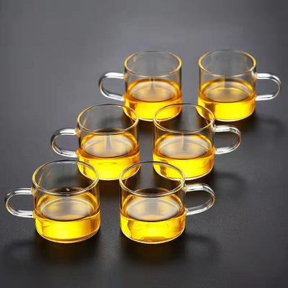 A beautifully arranged Thick Glass Transparent Tea Set, featuring a minimalist design with high borosilicate glass. The set includes six elegant tea cups and a matching cup holder, perfect for serving tea. Available in various sizes and styles, including transparent and colorful options with long spout pots.